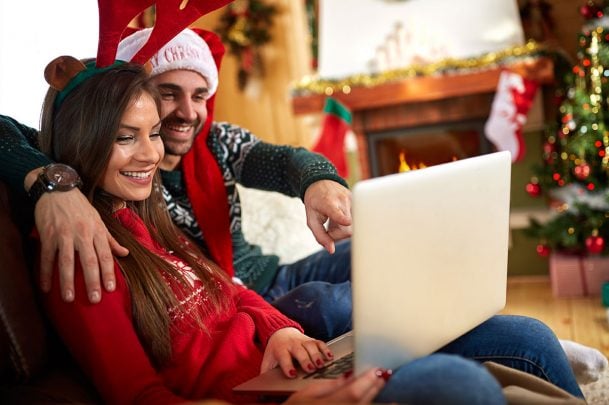 A man and woman dressed in holiday clothes watching a movie on their laptop