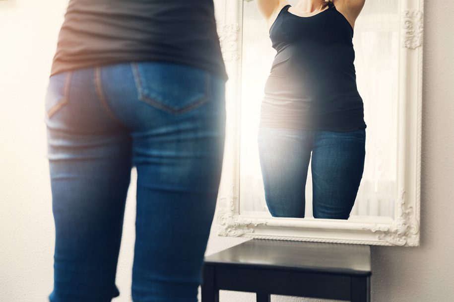 rear view of woman's torso as she looks in the mirror