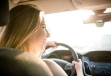 girl driving in car with a smile and sunshine coming through the window