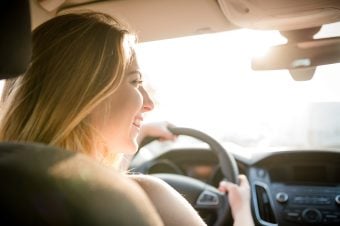 girl driving in car with a smile and sunshine coming through the window