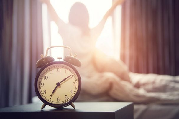 woman stretching by a sunlit window after her alarm goes off