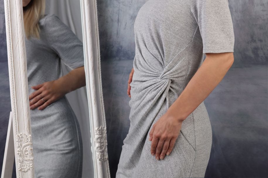 Woman in gray dress looking in the mirror - how to love your body shape