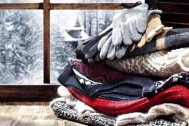 Stack of sweaters and gloves in front of a frosted windowpane