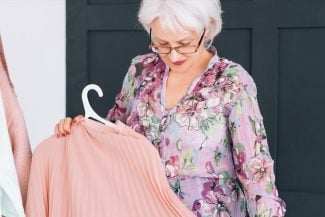Woman with white hair and glasses looking down at a pink shirt on a hanger