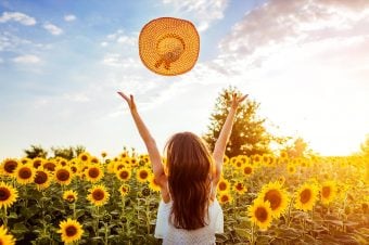 Woman throwing hat up in the air in a field of sunflowers
